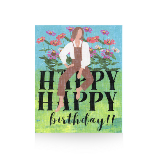 This greeting card features an oversized "HAPPY HAPPY birthday" greeting with a blue sky and grass background.  There is a modern illustrated lady in brown bib overalls and a white blouse sitting on the HAPPY word.  Behind her is a string of illustrated zinnia flowers.