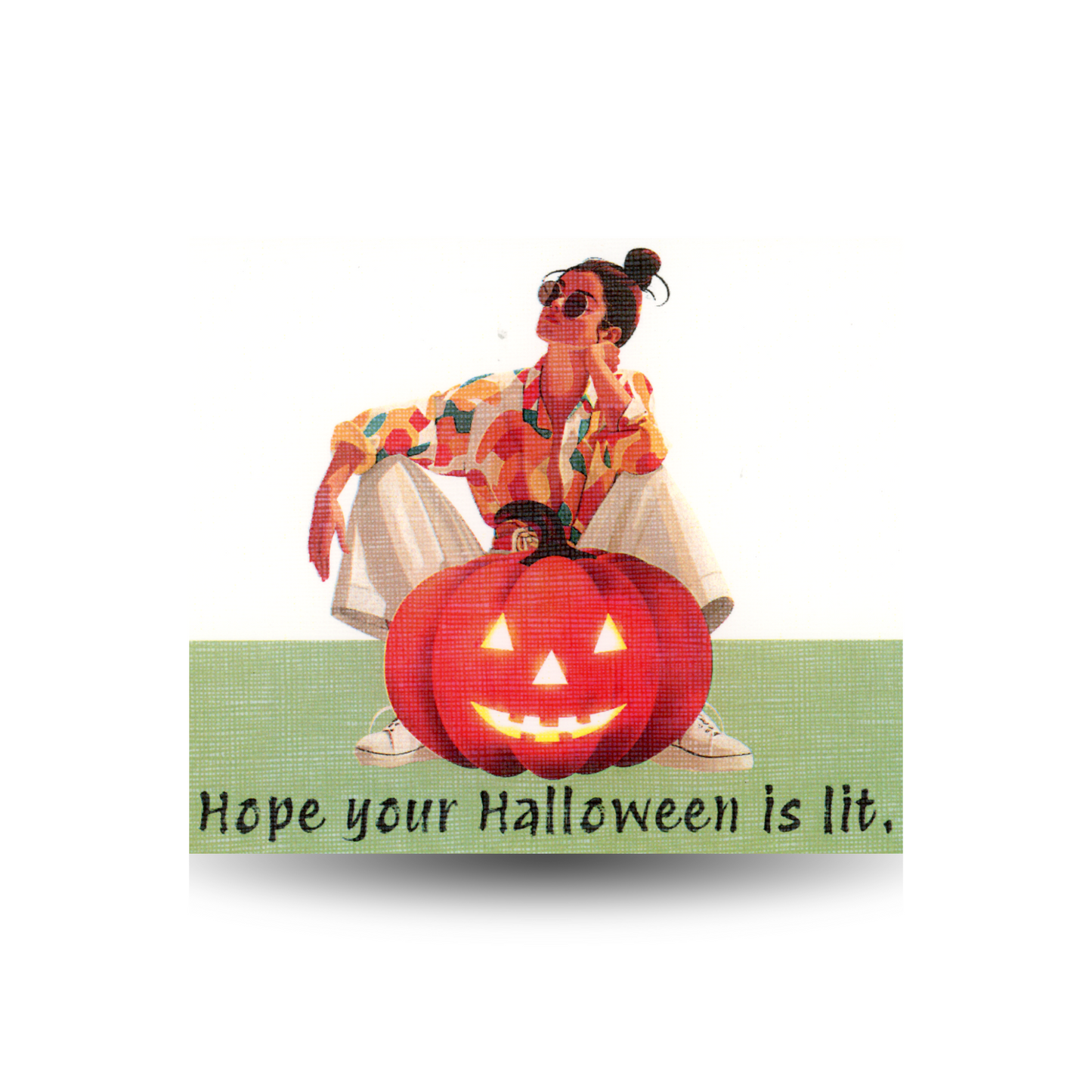This Halloween card features the greeting "Hope your Halloween is lit" and shows a modern woman in light-colored slacks, tennis shoes, and a print blouse crouching behind a large lit jack-o-lantern.  The background is white and the ground is green.  The greeting appears across the bottom of the card