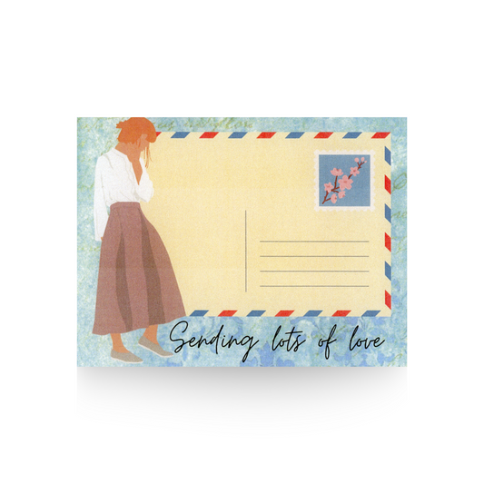 This greeting card features a blue printed background, upon which a vintage postcard is layered and to the left side of the postcard is a modern lady in a mauve skirt and long-sleeved white blouse.  The message "Sending lots of love" is written on the bottom part in cursive font