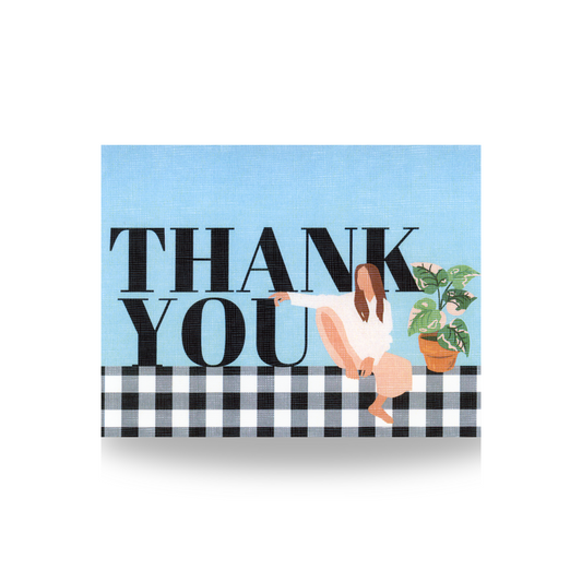 This THANK YOU greeting card features that sentiment in upper case large letters with a woman sitting on a black gingham border with one leg propped up and her arm stretched out over the lettering.  To the right of her is a variegated plant in a terra cotta pot.  The background is blue