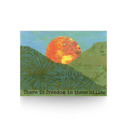"There is freedom in these hills" greeting card features a collaged hill scene made from printed papers and a hand-painted blue sky.  A large orange sun that is a vintage map is rising up between the two hills.  The message "There is freedom in these hills" is at the base of the card