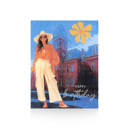 This Happy Birthday card features Woodburn Hall on the campus of West Virginia University with a modern illustrated woman standing on the left of the card in front of the building.  She is wearing white wide-legged pants and sandals and a tan top.  She has long brown hair and is wearing sunglasses and a white hat.  There is a retro yellow flower in the top right hand corner of the card.  Happy Birthday is written in the bottom right hand side of the card