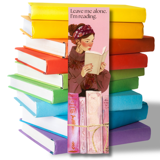 Colorful stack of books with a bookmark featuring a woman reading and the text 'Leave me alone, I'm reading.'